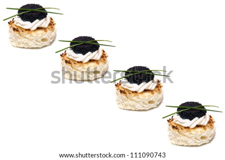 Appetizers: Finger Food - Row of black caviar canapes on base of toasted bread and butter, decorated with chive, isolated on white background.