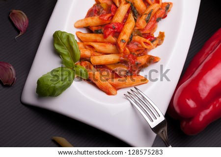 Italian typical recipes - Penne rigate with peppers sauce, decorated with fresh peppers and pitcher with flowers.