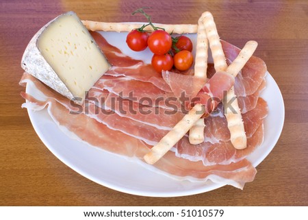 Food & Drinks - plate with italian appetizers: ham, Lagrein wine infused cheese, bread-sticks and cherry tomatoes.