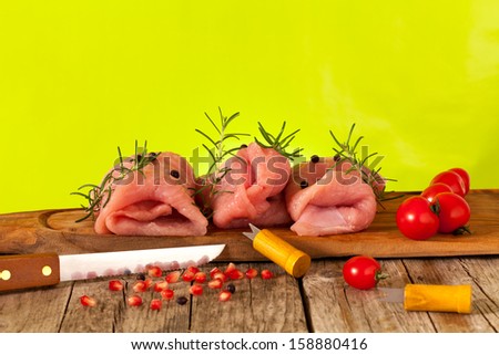 Wooden board with pieces of raw turkey meat, decorated with cherry tomatoes, rosemary, juniper berries and pomegranate.