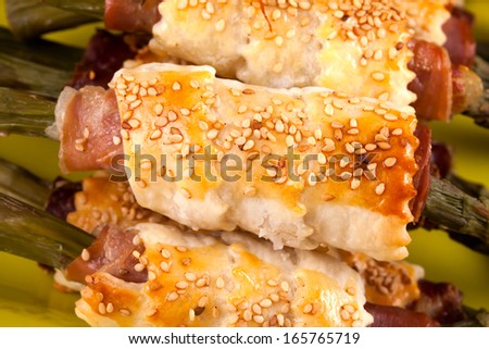 Closeup of asparagus rolls with prosciutto and puff pastry, decorated with sesame seeds.