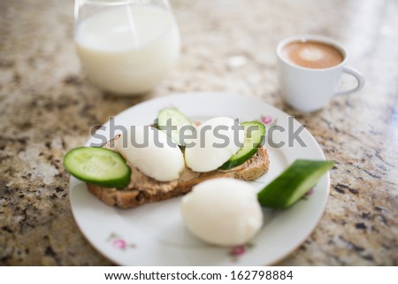 Healthy Breakfast Sandwich on a white plate with brown wheat bread milk cup of espresso and coffee.