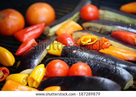 Grilled veggies including red peppers, eggplants, tomatoes, yellow peppers on wood-fire grill