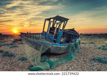 An old abandoned wooden fishing boat with nets washed up on a shingle beach, vintage effect