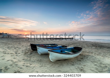 Stunning sunrise over a row of fishing boats on Bournemouth beach in Dorset, with the pier in the far distance