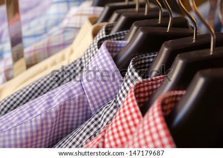 Men\'s plaid shirts in different colors on hangers in a retail shop