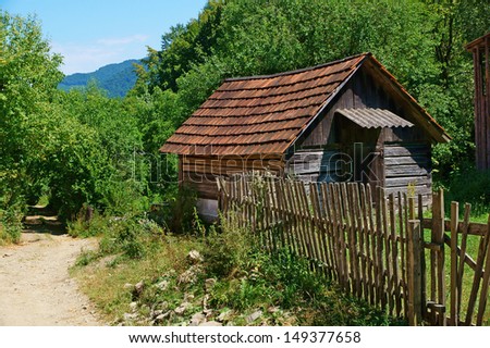 Old wooden rural house under shingles roof and fence by the mountain road