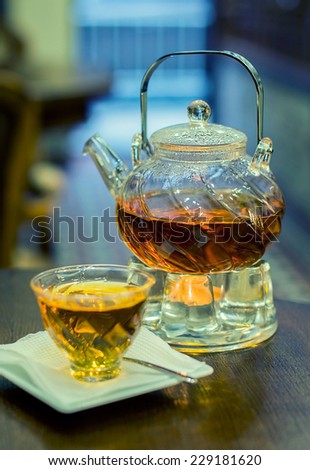 Glass teapot and cup with tea reheated with a candle on a wooden cafe table