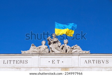 The upper part of Lviv Polytechnic National University main building (Lviv, Ukraine) with motto, sculptures of three muses and National Flag of Ukraine waving in the wind on blue sky background.