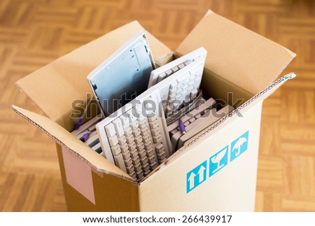 Office move concept - cardboard box with lots of computer keyboards on the wooden floor