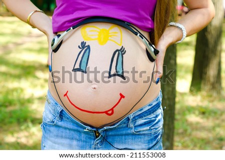 On the abdomen of a pregnant woman painted smiling face of her unborn daughter