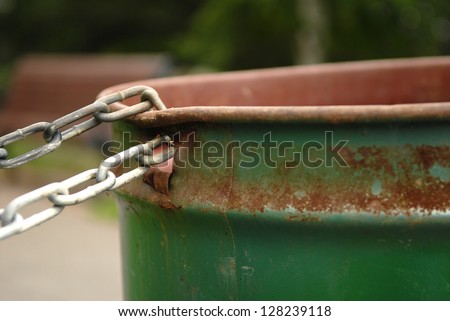 Image of a chained rusted garbage can in a park. Selective focus on where the chain is connected to the garbage can. Lots of space for content.