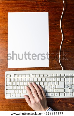 Female hands typing on a white keyboard next to a white paper on wooden background