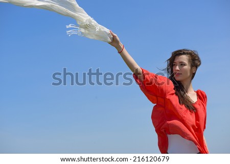 Happy young woman holding white scarf with opened arms expressing freedom, outdoor shot against blue sky. Beauty Girl Outdoors enjoying nature.