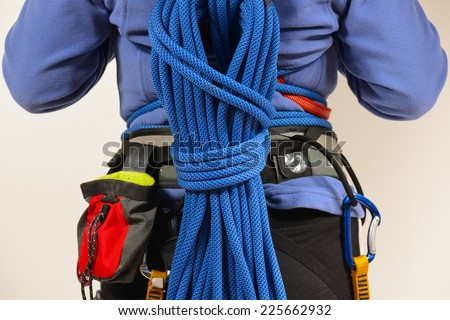 Young female rock climber wearing safety harness with climbing tools and climbing rope