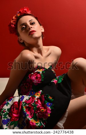 Fashion portrait of a redhead woman with flowers in hair. Attractive redhead woman posing on red background. Sexy woman