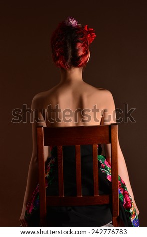 Fashion portrait of a redhead woman with flowers in hair, sitting on wooden chair. Attractive redhead woman. Fashion portrait of a redhead woman posing as Frida Kahlo. Close up portrait. Studio shot