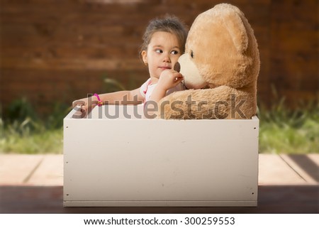 Beautiful little girl inside white wooden box with toy bear pretending to be in a car. Little girl having fun playing