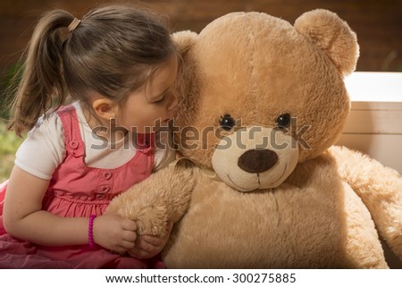 Outdoor portrait of expressive little girl kissing huge plush bear. Little girl playing with teddy bear