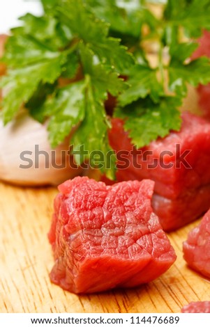 Raw  beef cubes on board with greens