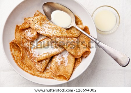 Sweet pancakes on plate with condensed milk on table