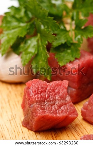 Raw fresh beef cubes on board with greens