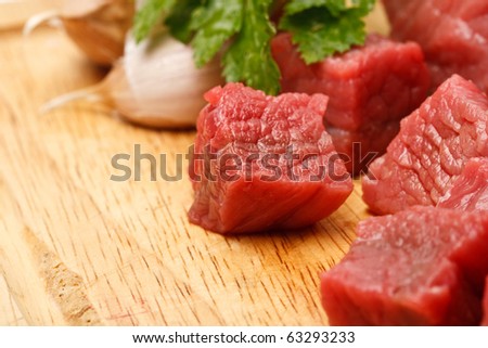 Raw fresh beef cubes on board with greens