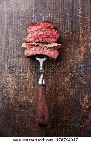 Slices of beef steak on meat fork on wooden background