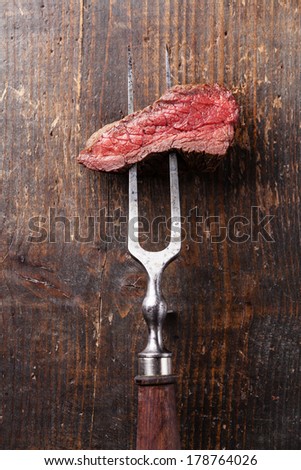 Piece of beef steak on meat fork on wooden background