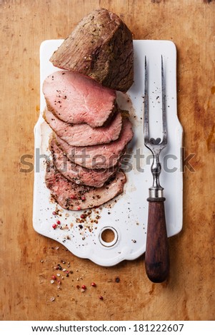 Roast beef and meat fork on wooden background