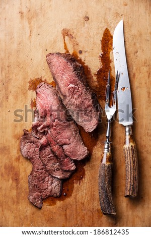 Roast beef with knife and fork for meat on wooden background