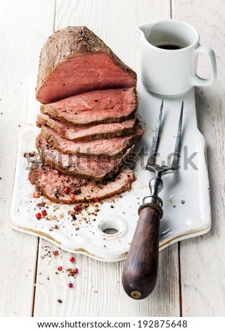 Roast beef with sauce and meat fork on white wooden background