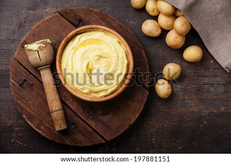 Wooden bowl with mashed potatoes and raw potatoes on dark background