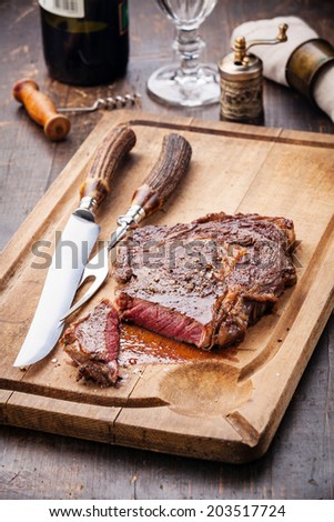 Medium rare grilled Beef steak Ribeye with knife and fork for meat on cutting board on dark wooden background