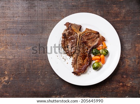Grilled T-Bone Steak  with vegetables on white plate on dark wooden background