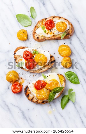 Bruschetta with roasted tomatoes and mozzarella cheese on grilled crusty bread on white marble