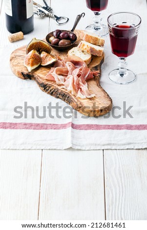 Prosciutto ham, Olives and red Wine on olive wood cutting board