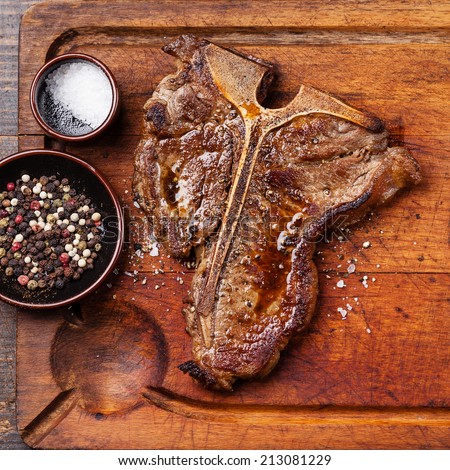 Grilled T-Bone Steak with salt and pepper  on meat cutting board on dark wooden background close up