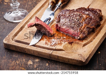 Steak Ribeye with knife and fork for meat on cutting board on dark wooden background
