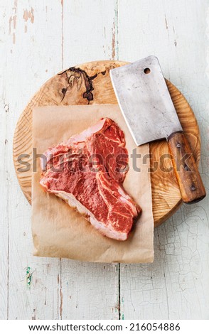 Raw fresh meat T-Bone Steak and meat cleaver on cutting board on blue background