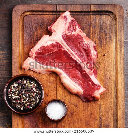 Raw fresh meat T-Bone Steak with salt and pepper on cutting board on dark wooden background