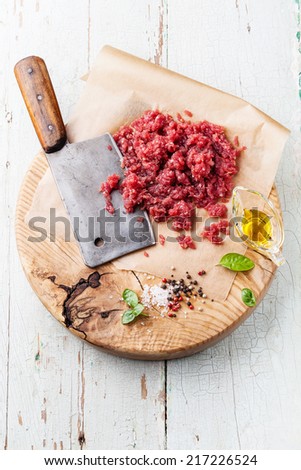 Raw chopped meat and meat cleaver on wooden cutting board on blue background