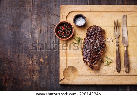 Grilled New York Striploin Steak with salt and pepper on meat cutting board on dark wooden background