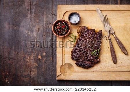 Grilled Ribeye Steak with salt and pepper on meat cutting board on dark wooden background
