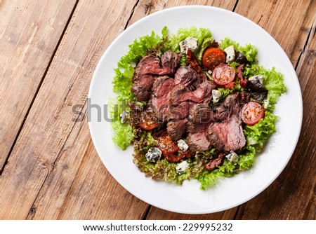 Salad leaves with sliced roast beef and sun-dried cherry tomatoes on wooden background