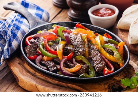 Beef Fajitas with colorful bell peppers in pan and tortilla bread and sauces