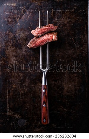 Slices of Rare beef steak on meat fork on dark background