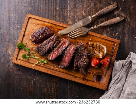 Sliced medium rare grilled Beef steak Ribeye with grilled onions and cherry tomatoes on cutting board on wooden background