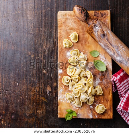 Homemade raw Tortellini and basil leaves on dark wooden background