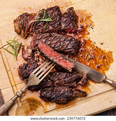 Grilled Ribeye Steak with with knife and fork on meat cutting board on wooden background
